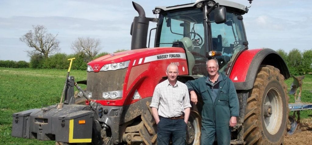 Two farmers in front of a tractor on a field