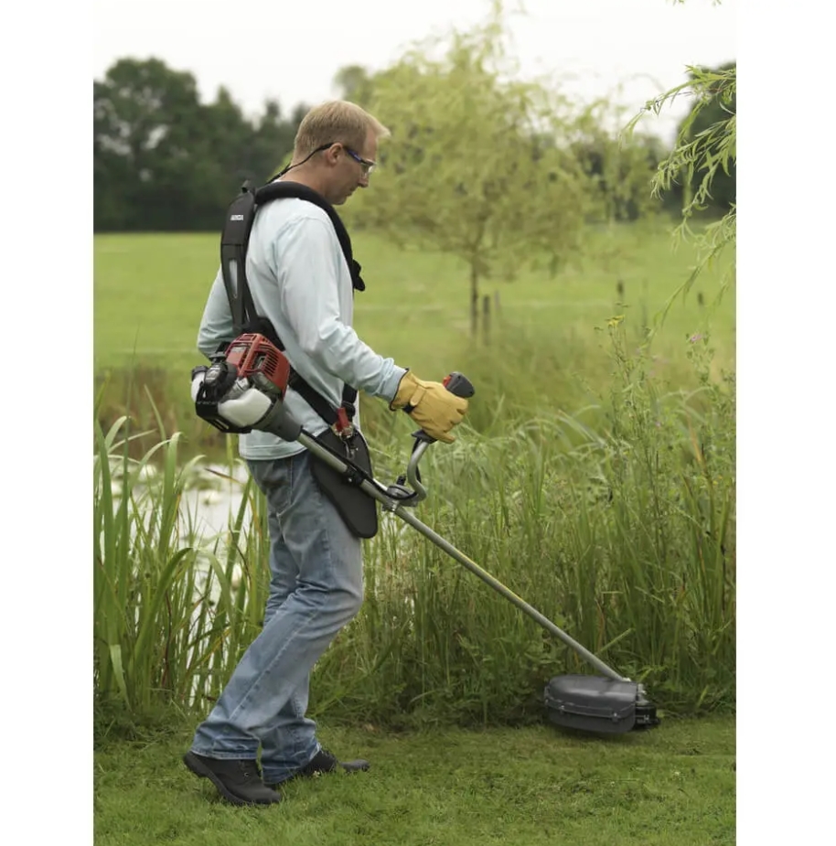 A man in safety glasses and gloves cuts long grass using a Honda Loop Handle Backpack Petrol Brushcutter.