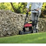 A man using a lawn mower on the grass in a garden next to a stone wall