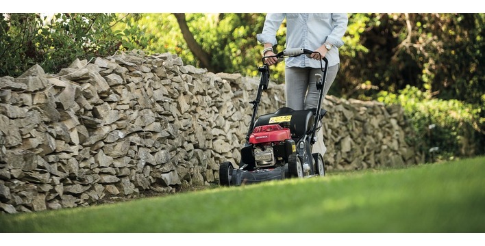 A man using a lawn mower on the grass in a garden next to a stone wall
