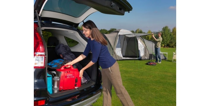 Woman removing a Honda EU10i Inverter Generator out of the back of car for camping in a field