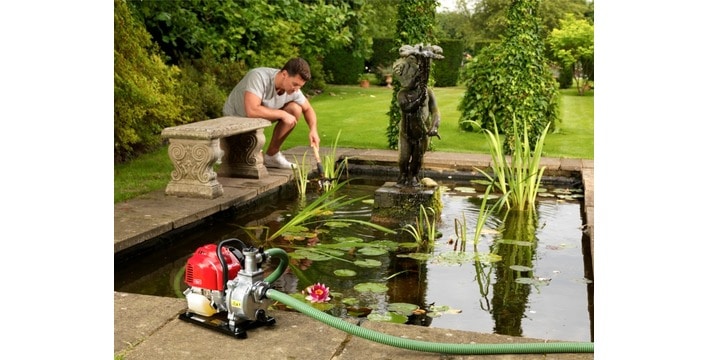 A man leans over his pond whilst the Honda WX10 Portable Water Pump is connected